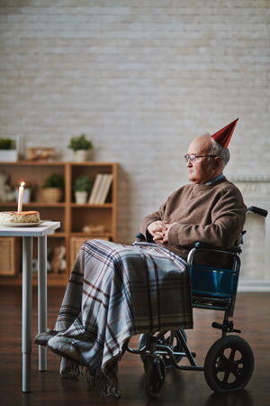 Senior man on wheelchair sitting in front of table with birthday cakeの写真素材
