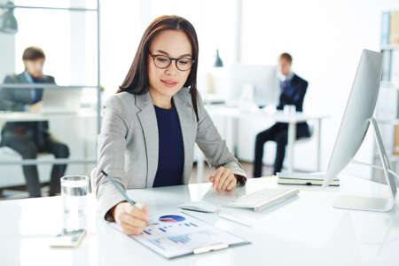 Pretty secretary analyzing data at workplace in front of computerの写真素材