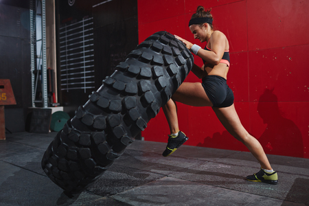 Active woman in sportswear flipping tyre in gymの写真素材