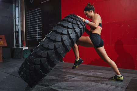 Active woman in sportswear flipping tyre in gym