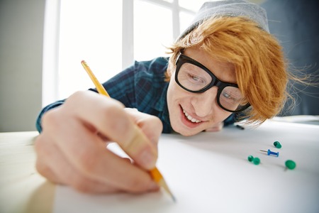 Happy young architect in eyeglasses drawing sketchの写真素材
