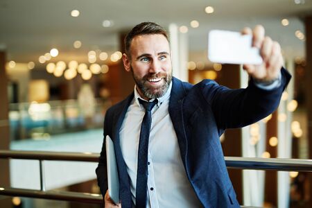 Happy businessman with gadget making his selfie indoors
