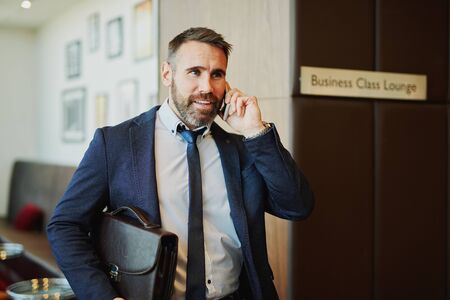 Successful employee with briefcase talking on the phone on the corner of lounge