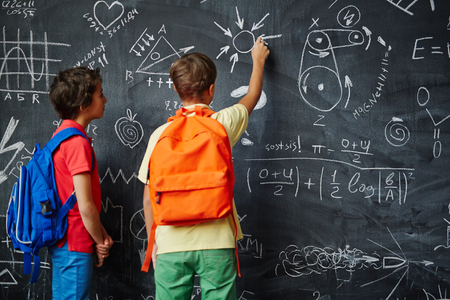Two boys with backpacks standing by blackboardの写真素材