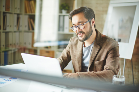 Young man in glasses working on his laptopの写真素材