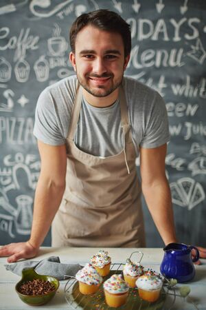Happy chef looking at camera behind counter of dessertsの写真素材