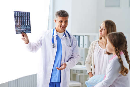 Male pediatrician explaining X-ray to child and her momの写真素材
