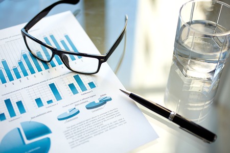 Glass of water, eyeglasses, pen and financial documentの写真素材