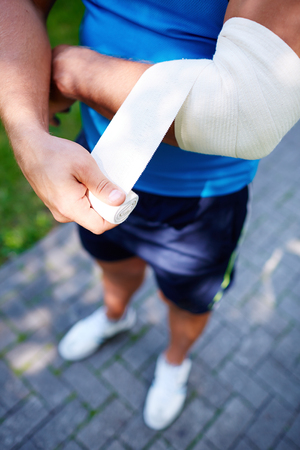 Young sportsman bandaging elbow joint outsideの写真素材