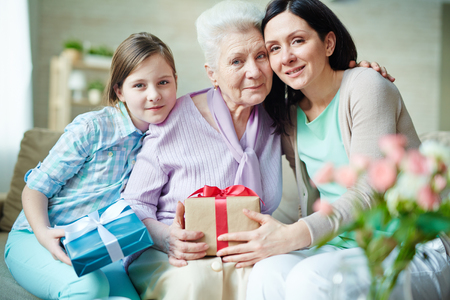 Young woman, elderly one and teenage girl with presents looking at cameraの写真素材