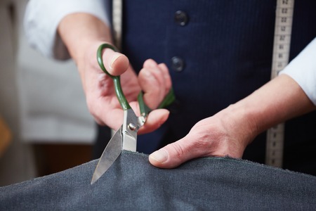 Hands of tailor with scissors cutting fabric