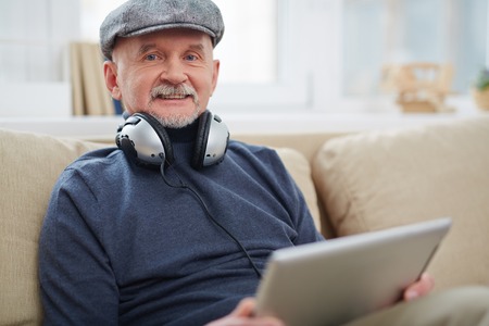 Portrait of senior man with headphone using touchpad