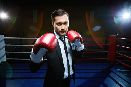 Powerful businessmen in suit and boxing gloves standing on boxing-ringの写真素材