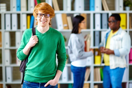 Handsome student in green pullover looking at camera in libraryの写真素材