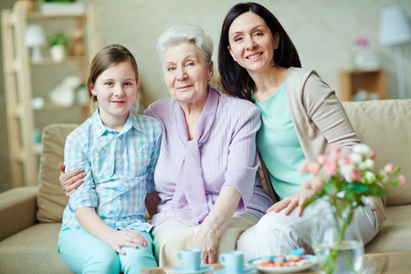 Happy young woman, elderly one and teenage girl sitting on sofaの写真素材