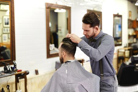 Young barber styling hair of a manの写真素材