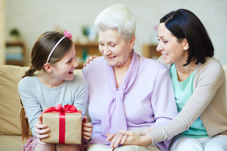 Young and elderly women looking at gift-box held by teenage girlの写真素材