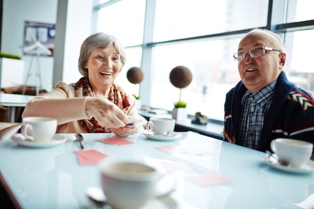Group of friendly seniors playing cards by tableの写真素材