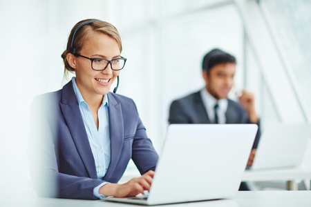 Pretty operator consulting clients online with colleague on backgroundの写真素材