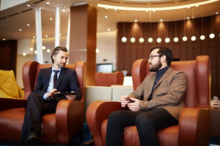 Two successful businessmen discussing plans or news in lounge of modern office centerの写真素材