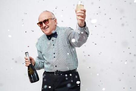 Happy senior man with bottle and flute of champagne looking at camera at partyの写真素材