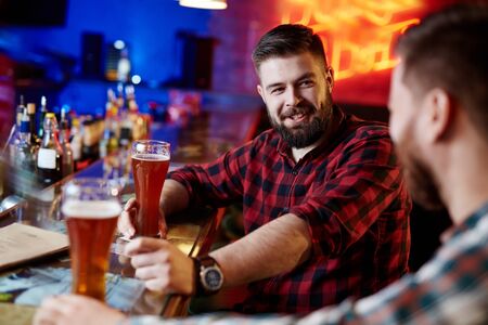 Happy bearded man with beer talking to his friend in pubの写真素材