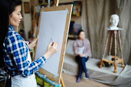 Young student drawing face of girl with pencil in workshopの写真素材
