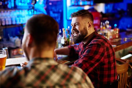 Happy bearded man and his friend sitting in pub
