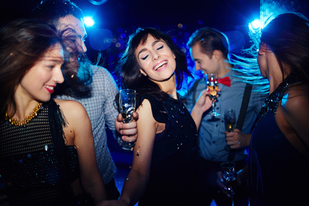 Ecstatic young woman dancing in night club among her friendsの写真素材