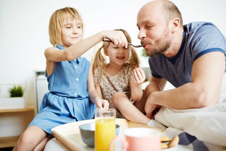 Little girl feeding her dad from spoon in the morning of father dayの写真素材
