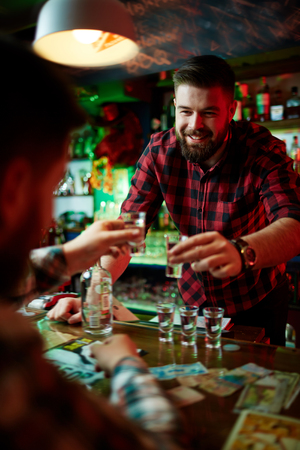 Happy barman and guy toasting with vodka over bar counterの写真素材