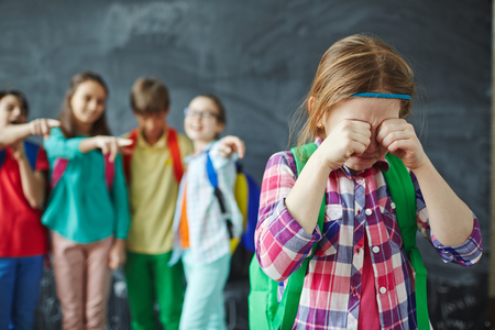 Schoolgirl crying while classmates teasing her on backgroundの写真素材