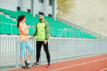 Sporty young couple in active-wear having talk at stadium