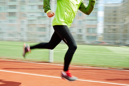 Blurred legs of young sportsman running on racetrack