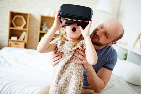 Father looking at his amazed daughter with vr headsetの写真素材