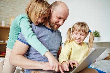 Girls and their father typing on laptop keypadの写真素材