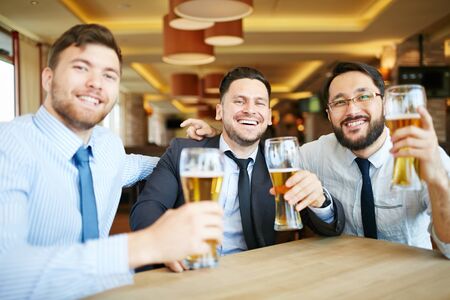 Happy businessmen with beer sitting in pubの写真素材