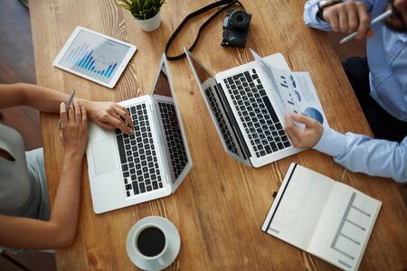 Workplace with gadgets, office supplies and two employees analyzing data
