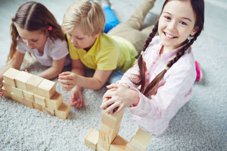 Cute girl playing bricks with her friends on backgroundの写真素材