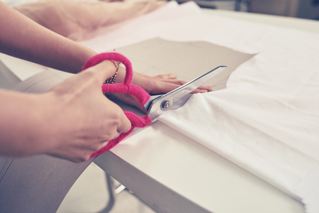 Hands of unrecognizable tailor woman cutting fabric with scissorの写真素材