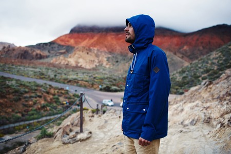 Young traveler in blue jacket standing by mountainの写真素材