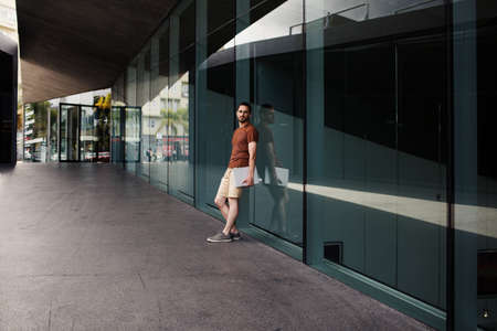 Man with laptop looking at camera by modern buildingの写真素材