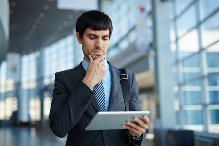 Pensive businessman networking with touchpad