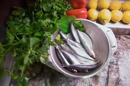 Fresh uncooked herrings in metallic bowl with parsley, peppers and lemons near byの写真素材