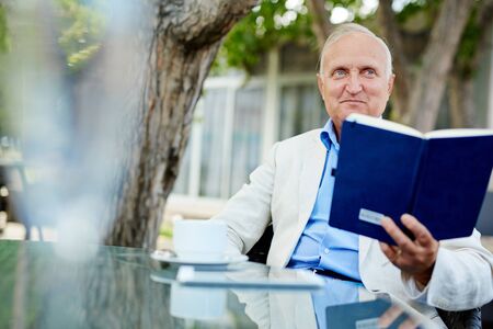 Senior man sitting at the table with his notebookの写真素材