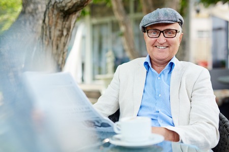 Smiling senior man sitting with newspaper at cafe outdoorsの写真素材