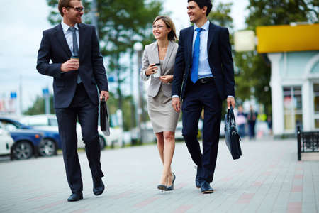Happy business people walking along the street and drinking takeaway coffeeの写真素材