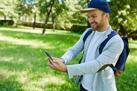 Smiling man with cellphone spending leisure in park