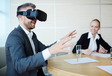 Modern businessman in virtual reality headset trying to touch something non-existent