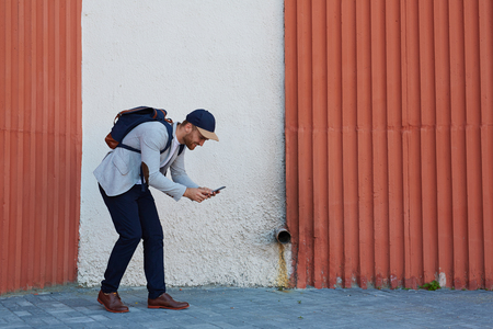 Contemporary active man playing popular mobile game in his smartphone outdoorsの写真素材